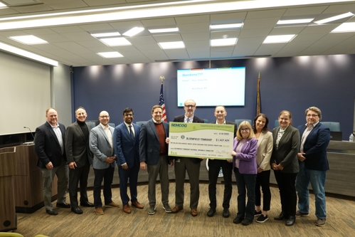Standing in front of the dais in Township Hall left to right: Corey Almas, PE, Township Director of Engineering and Environmental Services; Neal J. Barnett, Township Trustee; Christopher Kolinski, Township Trustee; Akaash Kolluri, Oakland County Office of US Senator Elissa Slotkin; Kevin Vettraino, Planning Director, SEMCOG; (Holding check: Mike McCready, Township Supervisor; Michael Schostak, Township Treasurer, SEMCOG Delegate; Sharon MacDonell, State Representative, District 56); - Samantha Steckloff, State Representative, District 19; Valerie Murray, Township Trustee; Mark Antakli, Township Trustee.