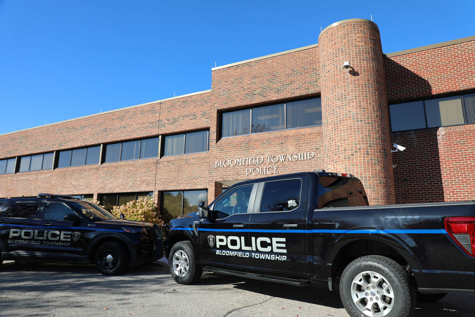 Two Bloomfield Township police vehicles parked nose to nose in front of the entrance to a 2 story brick building with lettering that reads Bloomfield Township Police.